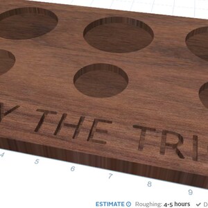 Puede incluir: Una bandeja de madera con seis huecos circulares para vasos o platos pequeños. La frase "TRY THE TRIO" está tallada en la madera. La bandeja es de color marrón cálido.