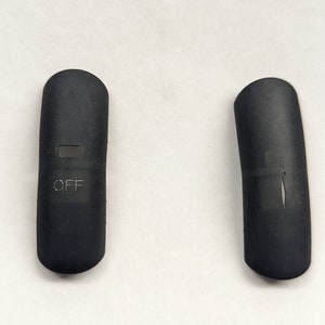 May include: Two black, oblong-shaped objects. One has the word "OFF" printed on it, along with a small rectangular indentation. The other object is curved and lacks any text. Both objects have a textured surface.