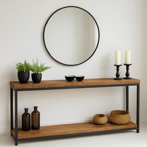 May include: A contemporary console table with a black metal frame and a natural wood top and shelf. The table is adorned with black pots with plants, black bowls, candles, and decorative bottles. A round black framed mirror hangs above the table.