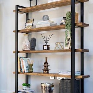 May include: A black metal and wood bookshelf with five shelves. The shelves are filled with books, decorative items, and plants. The bookshelf is against a white wall.