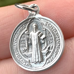 Puede incluir: Medalla de San Cristóbal de plata con una imagen detallada de San Cristóbal llevando al niño Jesús. La medalla tiene la inscripción "S. CHRISTOPHORO. PRO. TE. ORA" en el frente.