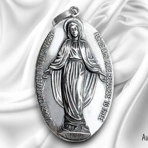 May include: Silver oval pendant featuring a detailed image of the Virgin Mary with the inscription "Our Lady Conceived Without Sin Pray For Us Who Have Recourse To Thee".