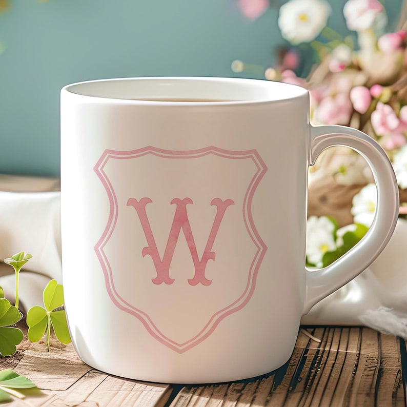 Pu&ograve; includere: Una tazza in ceramica bianca con un emblema rosa a forma di scudo sulla parte anteriore. Al centro dello scudo si trova una grande lettera W rosa stilizzata. La tazza presenta una finitura liscia e lucida e un manico curvo sul lato destro.