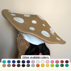 May include: A large mushroom hat with a tan cap and white spots. The underside of the hat is white. The image also shows a color palette of other available colors.