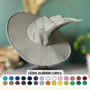 Può includere: Un cappello da strega grigio chiaro con tesa larga e corona a punta e piegata. Il cappello è realizzato in un materiale morbido e strutturato. L'immagine mostra anche una varietà di altri colori disponibili.
