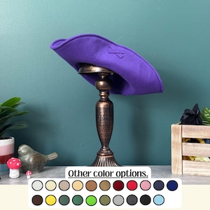 May include: A purple felt hat with a decorative bow detail, displayed on a bronze-colored stand. The hat has a wide brim and a slightly curved shape. The text "Other color options" is visible at the bottom of the image, along with a color palette.
