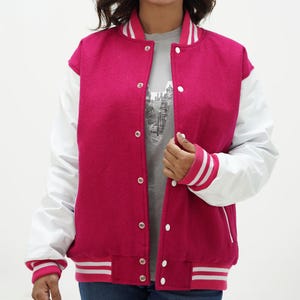 May include: A pink and white varsity jacket with a white zipper and white sleeves. The jacket has a ribbed collar, cuffs, and hem.