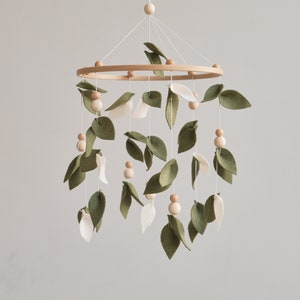 May include: A wooden baby mobile with green felt leaves and white felt flowers hanging from a wooden ring. The mobile is decorated with small wooden beads.