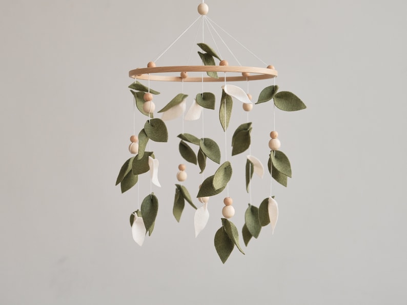 Whimsical olive leaf baby crib mobile with charming wooden embellishments, evoking the beauty of the forest, ideal for creating a serene nursery ambiance. This crib mobile will be a memorable baby shower gift or gift newborn.