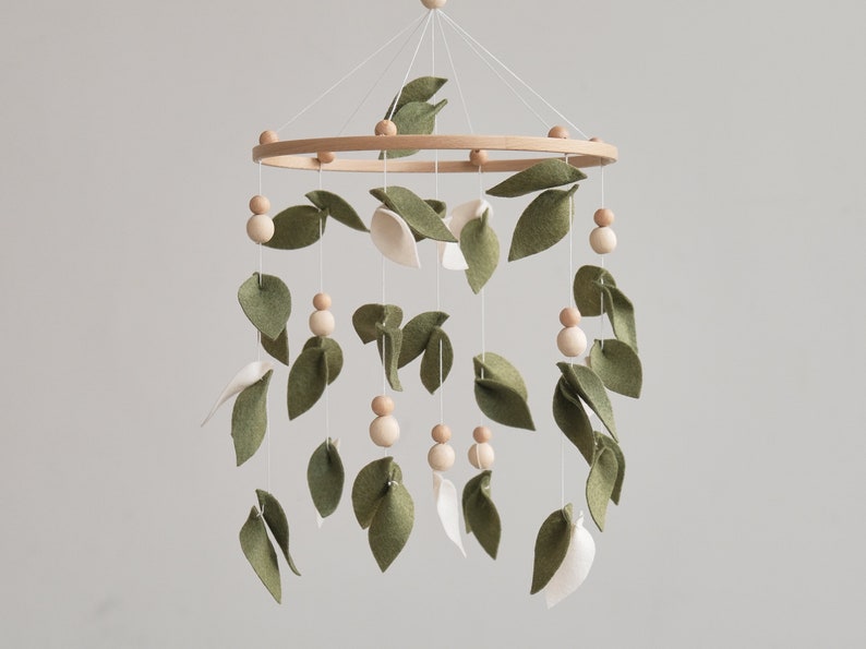 Handcrafted nursery mobile featuring rustic wooden balls and olive felt leaf, designed to complement a natural nursery decor with its earthy tones.