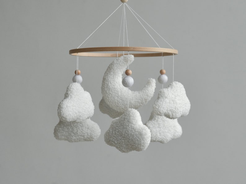 Handcrafted baby mobile made from bouclé, adorned with fluffy clouds, a crescent moon, and charming wooden balls. This baby crib mobile is a perfect neutral nursery decor.