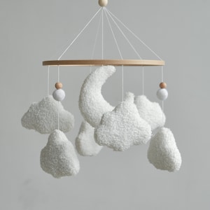 Whimsical bouclé nursery mobile with fluffy clouds, a crescent moon, and cute wooden balls, adding a touch of magic to boho nursery