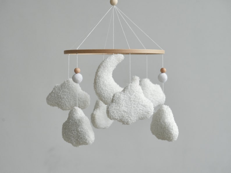 Whimsical bouclé nursery mobile with fluffy clouds, a crescent moon, and cute wooden balls, adding a touch of magic to boho nursery