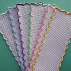 May include: Six white fabric bookmarks with scalloped edges. The bookmarks are trimmed in different colours: purple, light blue, green, pink, and gold.