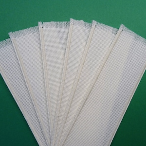 Peut inclure: Un ensemble de huit bandes de tissu en coton blanc avec des bords effilochés. Les bandes sont disposées en éventail sur un fond vert.