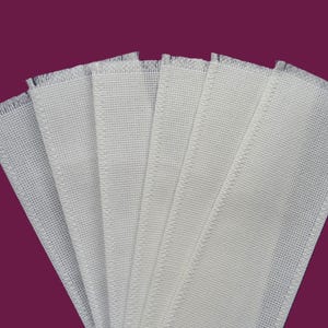 May include: A fan of several white rectangular fabric pieces with a woven texture. The edges are frayed, and the sides are stitched. The background is a solid dark purple.