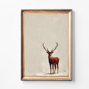 May include: A framed art print featuring a brown deer with large antlers standing in a snowy landscape. The artwork is set within a gold-colored, ornate frame, creating a vintage aesthetic. The background is a muted, off-white color.