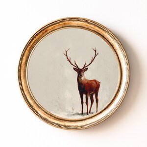 May include: A round wall art piece featuring a painting of a deer with large antlers. The deer is painted in shades of brown and red against a neutral background. The artwork is framed in a gold, ornate, circular frame.