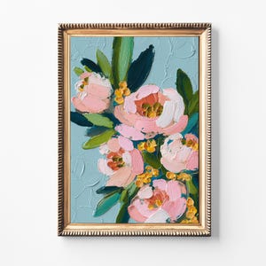 May include: A framed floral painting featuring pink and white peonies with green leaves and yellow accents against a light blue textured background. The gold frame adds a classic touch to the artwork.