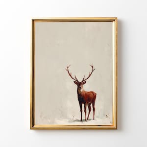 May include: A framed print featuring a majestic deer with large antlers. The deer is depicted in shades of brown and red against a muted, off-white background. The artwork is encased in a gold-colored frame, adding a touch of elegance.