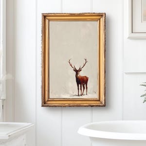 May include: A framed print of a deer with large antlers. The artwork is in a gold-colored frame and hangs on a white wall. The deer is brown with a light background. The overall theme is rustic and nature-inspired.