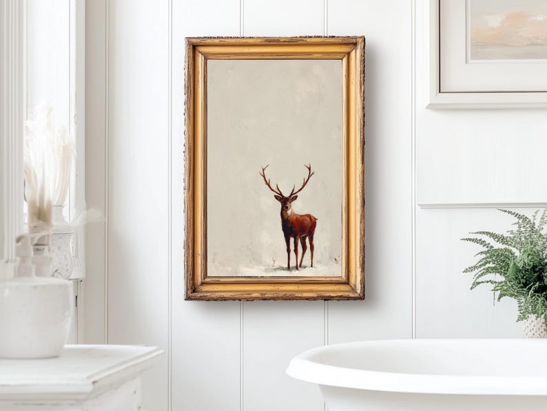 May include: A framed print of a deer with large antlers. The artwork is in a gold-colored frame and hangs on a white wall. The deer is brown with a light background. The overall theme is rustic and nature-inspired.