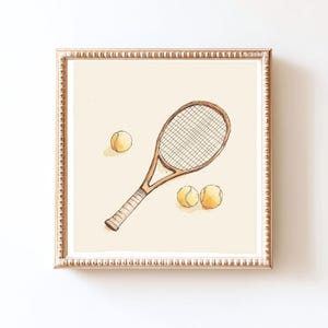 Puede incluir: Ilustración en acuarela de una raqueta de tenis y tres pelotas de tenis. La raqueta es marrón con un agarre blanco y una red. Las pelotas de tenis son amarillas. La obra de arte está enmarcada en un marco dorado.