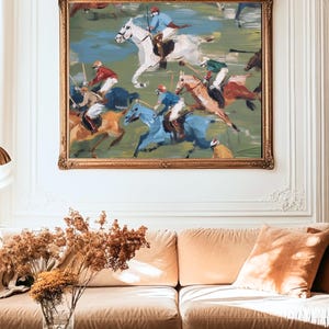 Puede incluir: Una pintura al &oacute;leo de un partido de polo en un marco dorado ornamentado. La obra representa jinetes con atuendos coloridos a caballo, compitiendo en un campo verde. La pintura cuelga sobre un sof&aacute; beige con cojines naranjas.