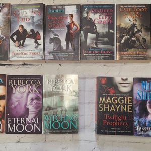 May include: A shelf of paperback books with various titles and authors. The books are arranged in two rows. The top row features books with titles like "Wicked Night", "One Foot in the Grave", and "Halfway to the Grave". The bottom row features books with titles like "Shadow of the Moon", "Eternal Moon", "Witching Moon", "Twilight Prophecy", "Embrace the Twilight", and "Night Bards".