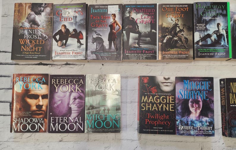 May include: A shelf of paperback books with various titles and authors. The books are arranged in two rows. The top row features books with titles like "Wicked Night", "One Foot in the Grave", and "Halfway to the Grave". The bottom row features books with titles like "Shadow of the Moon", "Eternal Moon", "Witching Moon", "Twilight Prophecy", "Embrace the Twilight", and "Night Bards".