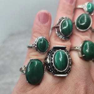Pode incluir: Um conjunto de seis an&eacute;is de prata com pedras ovais de malaquita verde. Os an&eacute;is s&atilde;o usados em uma m&atilde;o.