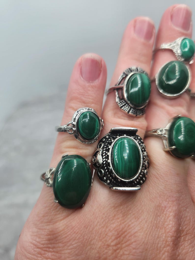 Pode incluir: Um conjunto de seis an&eacute;is de prata com pedras ovais de malaquita verde. Os an&eacute;is s&atilde;o usados em uma m&atilde;o.