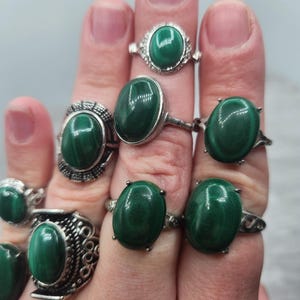 Pode incluir: Um conjunto de sete an&eacute;is de prata com pedras preciosas de malaquita de forma oval. Os an&eacute;is s&atilde;o usados em uma m&atilde;o, mostrando as pedras verdes.