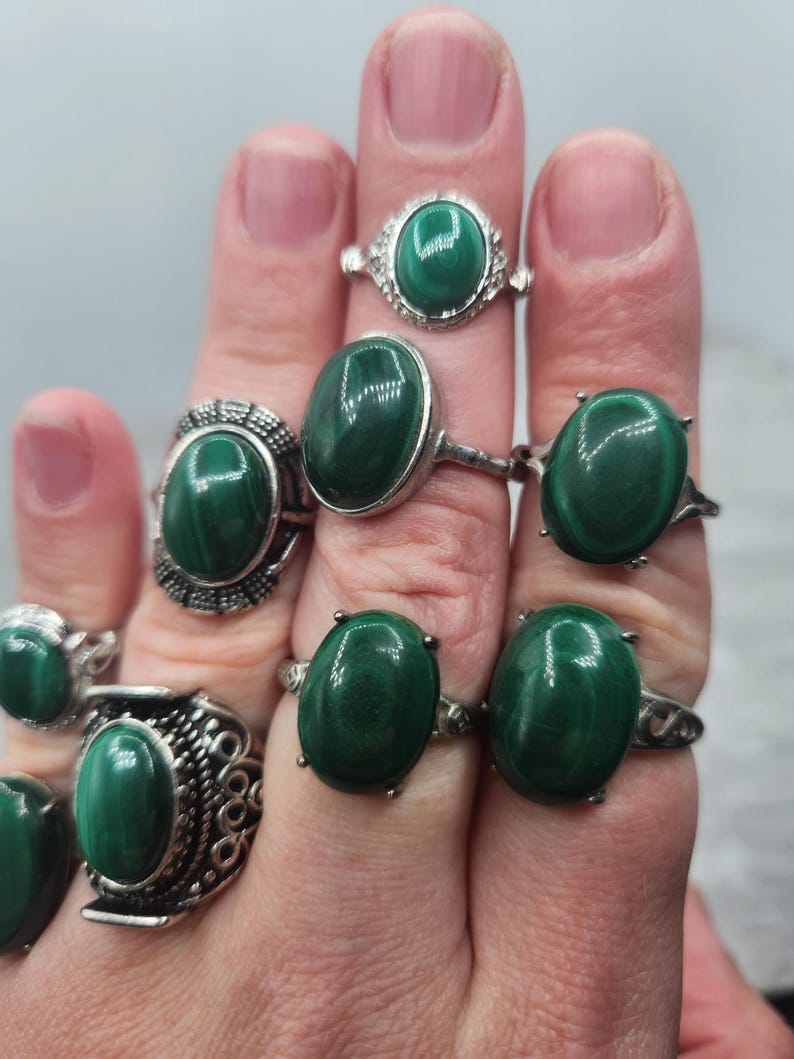 Pode incluir: Um conjunto de sete an&eacute;is de prata com pedras preciosas de malaquita de forma oval. Os an&eacute;is s&atilde;o usados em uma m&atilde;o, mostrando as pedras verdes.