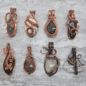 May include: Assortment of eight copper wire wrapped pendants with various natural stone and glass inlays. Each pendant features a unique design and color combination.