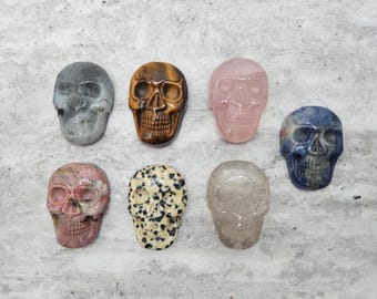 May include: Collection of carved gemstone skulls in various colors and patterns. Includes a gray skull, a tiger's eye skull, a pink rose quartz skull, a blue sodalite skull, a pink rhodonite skull, a dalmatian jasper skull, and a clear quartz skull.