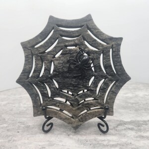 May include: A gray and black marble spider web sculpture with a black spider in the center. The sculpture is on a black metal stand.