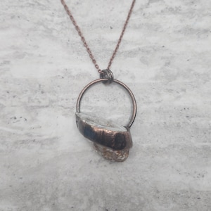 May include: A copper necklace with a unique pendant featuring a white stone encased in a copper ring.