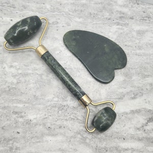 May include: A green jade roller and gua sha set. The roller has a gold handle and two green jade rollers. The gua sha is a heart-shaped green jade tool.