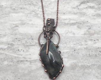May include: A copper necklace with a dark grey labradorite stone pendant and a copper bird skull charm.