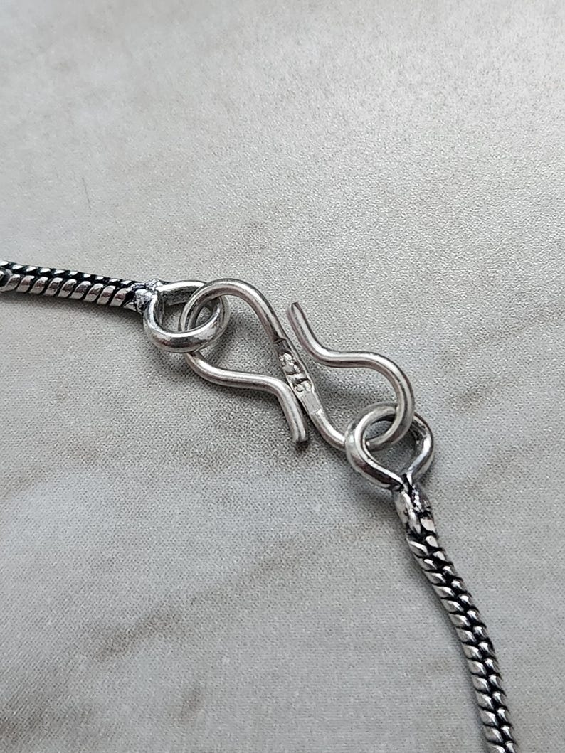 Peut inclure: Gros plan sur un fermoir de collier en argent. Le fermoir est de style crochet et &oelig;illet, avec une petite boucle &agrave; une extr&eacute;mit&eacute; et un crochet incurv&eacute; &agrave; l'autre. La cha&icirc;ne est de style serpent.