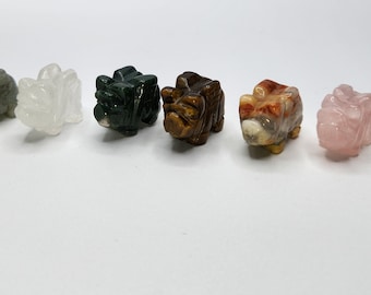 May include: Seven small carved rhinoceros figurines made of different types of stone. The figurines are arranged in a row from left to right. The stones are grey, white, green, brown, orange, pink, and green.