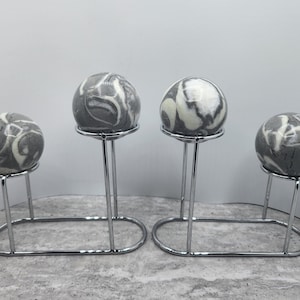 May include: Three gray and white marbled spheres on silver stands. The spheres are on a gray surface.
