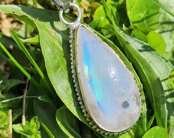 May include: A teardrop-shaped pendant necklace with a silver chain. The pendant features a large, iridescent moonstone set in a silver bezel. The moonstone displays a range of colors, including blue and green, and is surrounded by a detailed silver border.