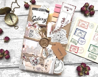 May include: A vintage-themed gift set with a compass, dried roses, and a wrapped package. The package is adorned with a wax seal, twine, and decorative paper with the text "Galaxy" and "Admit One". Includes a ticket, stickers, and a tag that says "Romance".