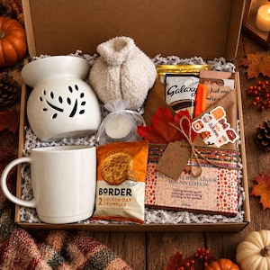 May include: A gift box containing a white ceramic wax warmer, a white speckled mug, a pair of fuzzy socks, a tea light candle, a pack of Border Golden Oat Crumbles, a Galaxy chocolate bar, a book wrapped in brown paper, and autumn stickers.