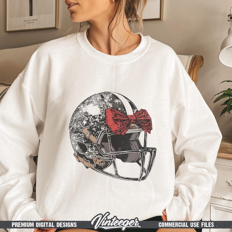Puede incluir: Sudadera blanca con un dise&ntilde;o de casco de f&uacute;tbol americano. El casco tiene un patr&oacute;n de bola de discoteca y un lazo rojo. La sudadera tiene el texto "Vinteeger" en la parte inferior. Es un dise&ntilde;o digital premium.
