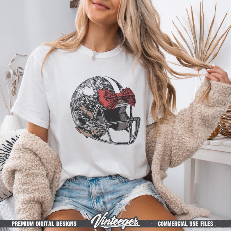 Puede incluir: Camiseta blanca con un dise&ntilde;o de casco de f&uacute;tbol con un lazo rojo. El casco tiene un patr&oacute;n en blanco y negro y una m&aacute;scara facial marr&oacute;n. La camiseta tiene el texto "Vinteeger" en la parte inferior.