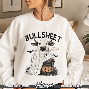 May include: White sweatshirt with a Halloween-themed graphic. The design features a cow dressed as a ghost, holding a jack-o'-lantern, with the text "BULLSHEET" above and "MOO... I MEAN BOO" below. Includes bat silhouettes.