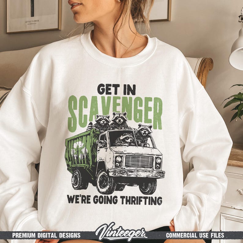 Puede incluir: Sudadera blanca con un gr&aacute;fico de mapaches en un cami&oacute;n con el texto "GET IN SCAVENGER WE'RE GOING THRIFTING". El dise&ntilde;o es en negro y verde.